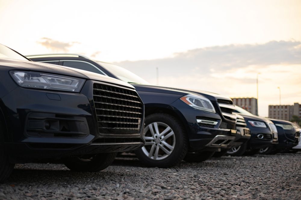 Row of parked black cars on a gravel lot at sunset