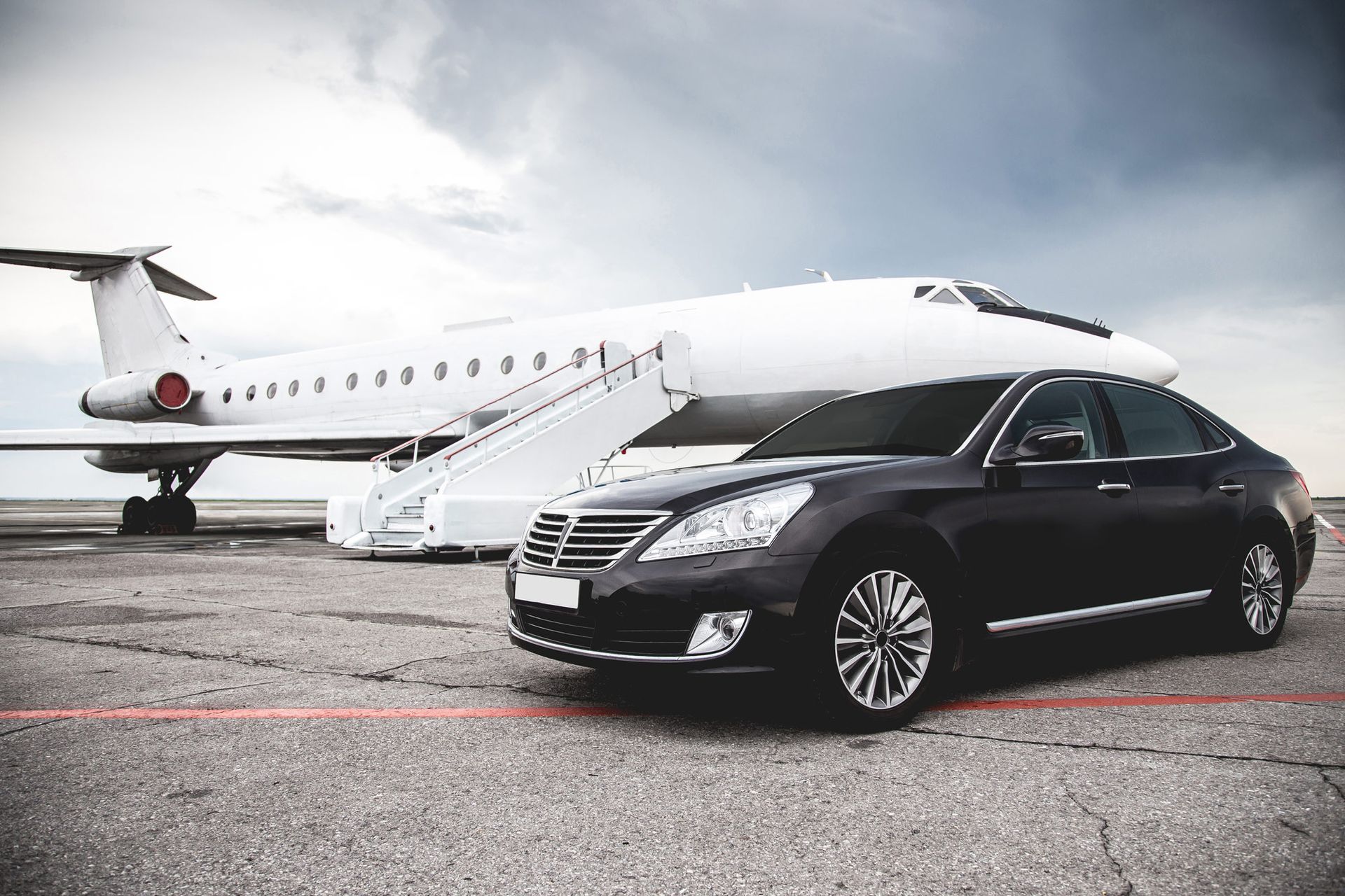 Black luxury sedan parked beside a private jet on an airport tarmac