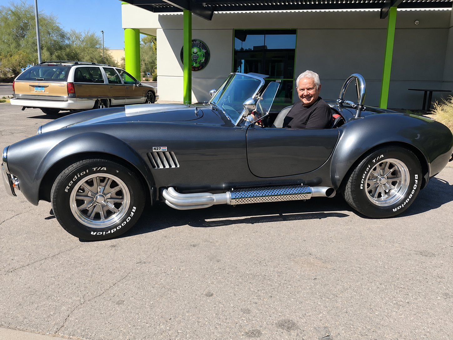Person smiling in a blue convertible sports car parked outside a garage