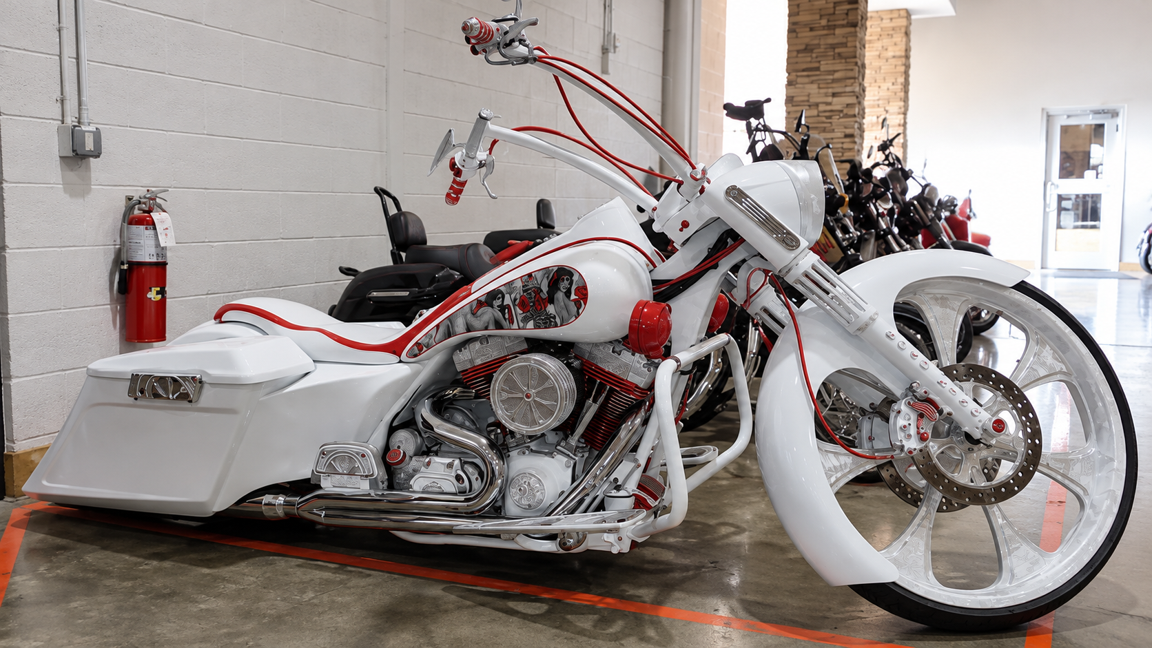 Custom white-and-red chopper motorcycle displayed indoors on a red carpet, with a fire extinguisher nearby