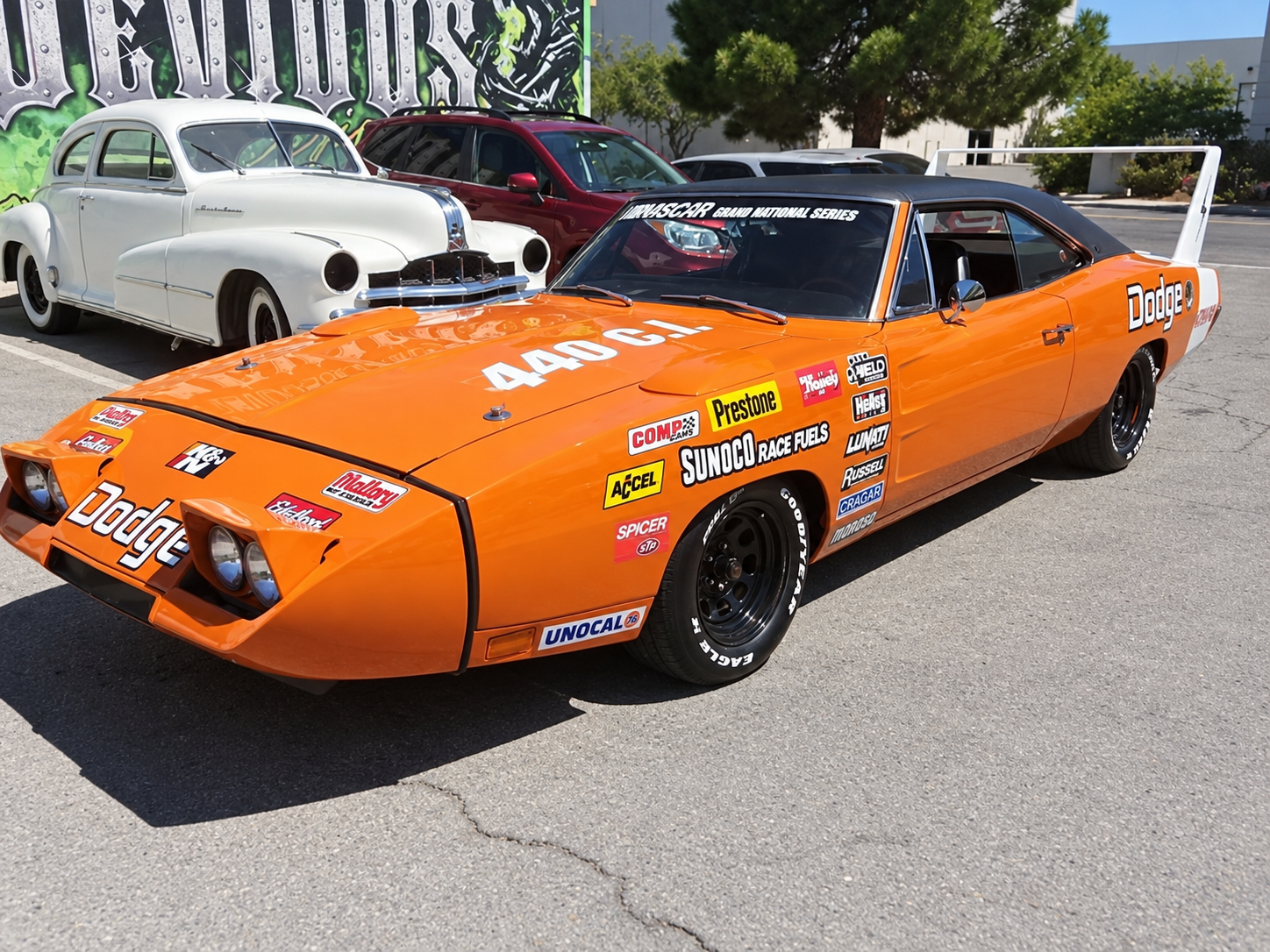 Orange vintage Dodge muscle car with racing decals parked outdoors at a car show