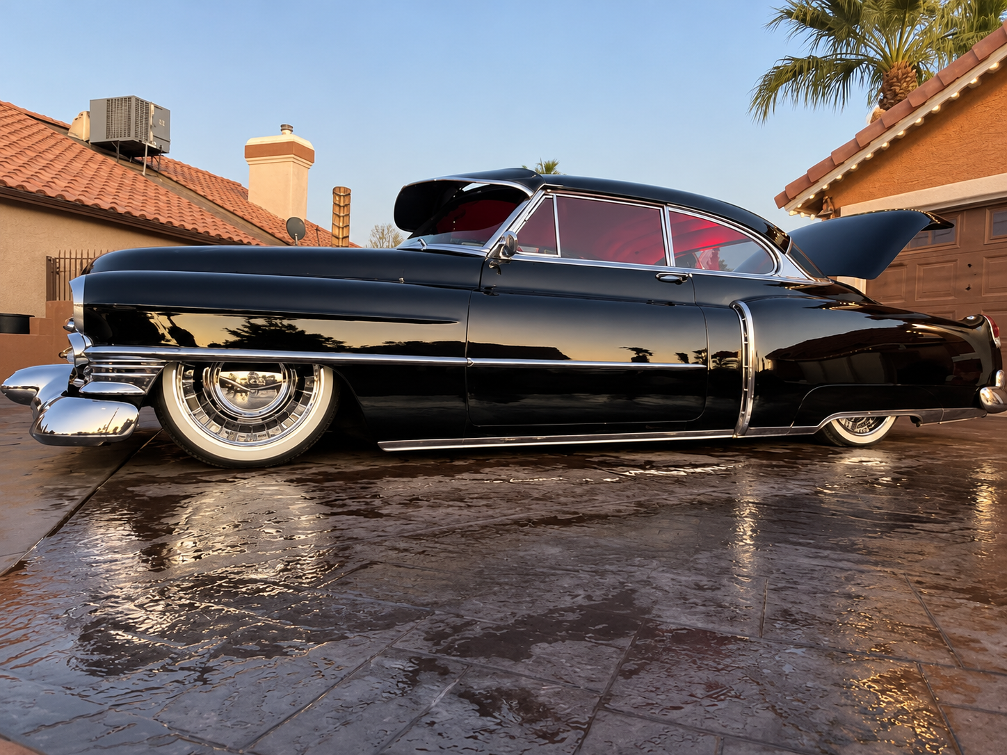 Black classic lowrider car parked in a driveway, with red interior and chrome accents.