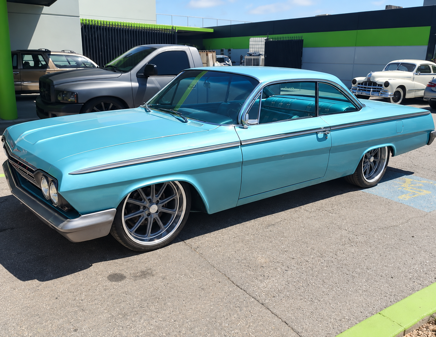 Turquoise classic coupe parked outdoors in a sunny lot, with chrome trim and black rims