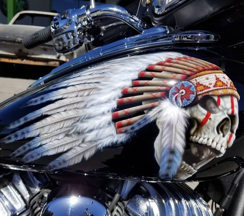 Chrome motorcycle tank with a Native American skull and feather mural in white, red, and blue