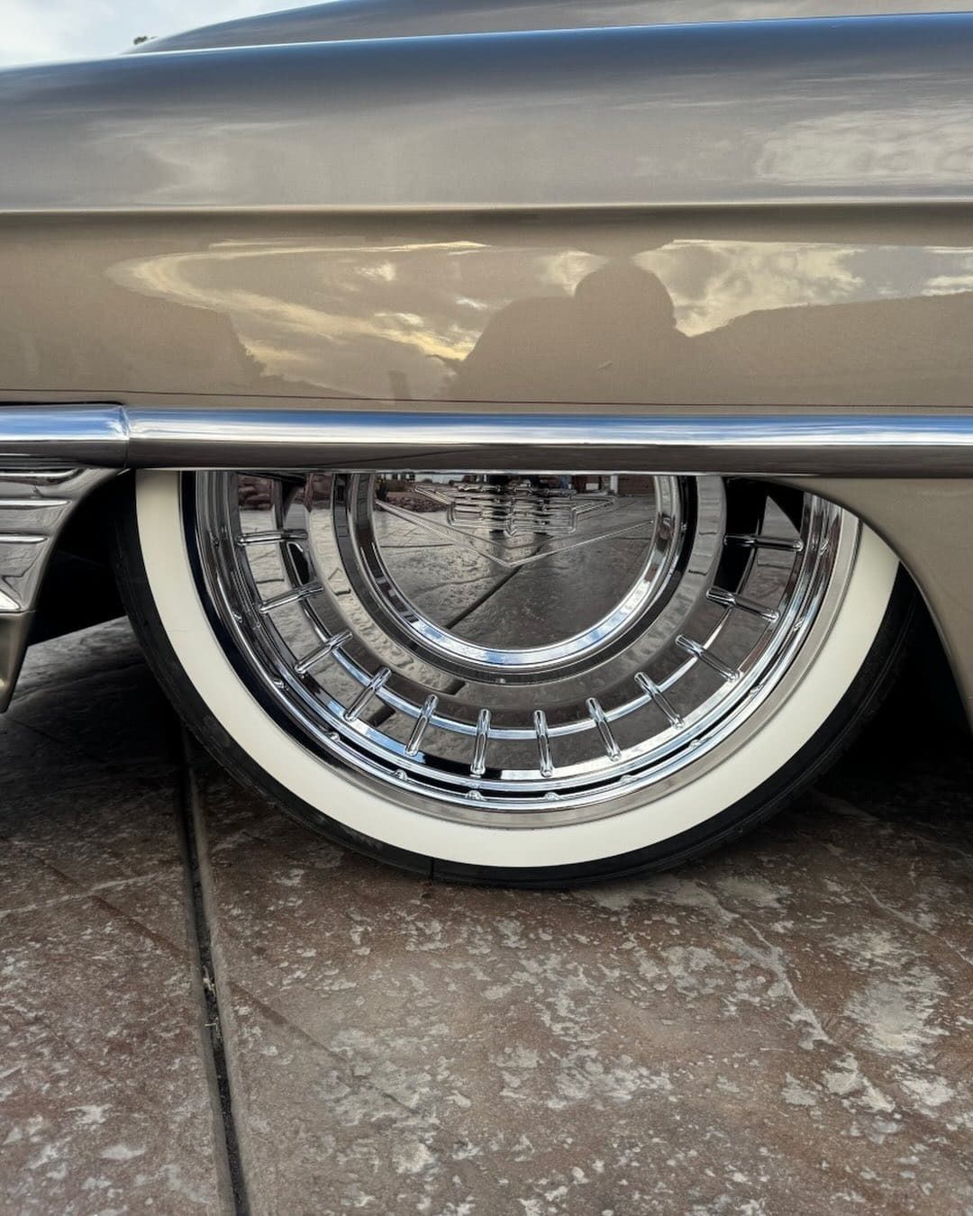 Close-up of a chrome wire wheel with a whitewall tire under a silver classic car.