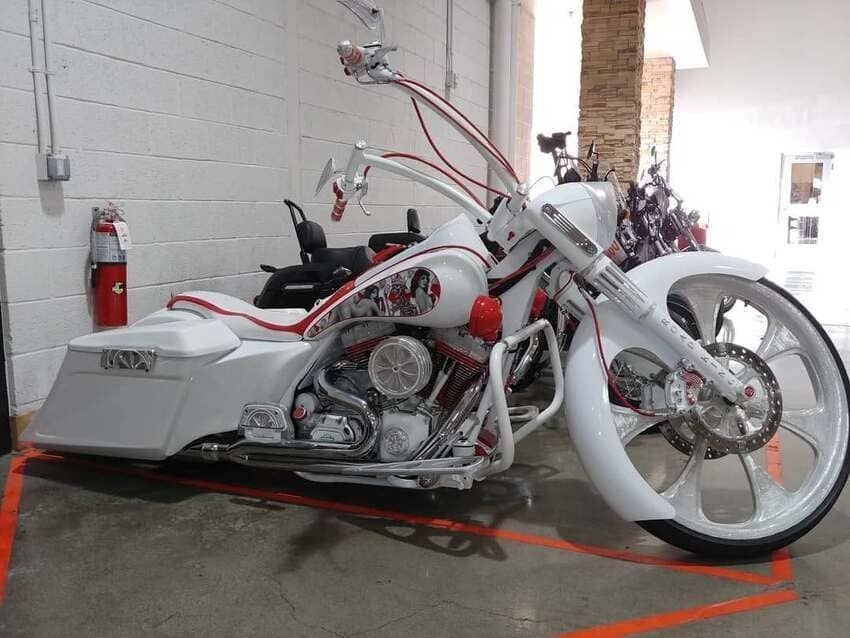 Custom white-and-red chopper motorcycle displayed indoors on a red carpet, with a fire extinguisher nearby
