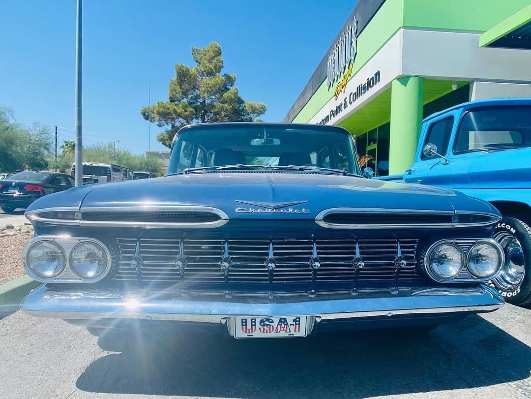 Front view of a black vintage car parked outside a building in bright sunlight