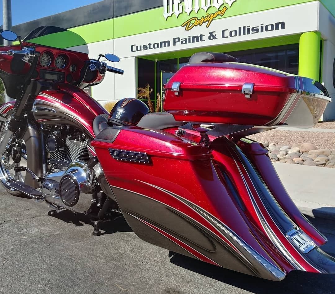 Two custom red motorcycles parked outside a custom paint and collision shop