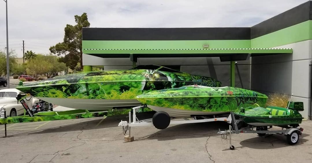 Green camouflage jet on pavement outside a building, with maintenance gear attached to its nose and fuselage.