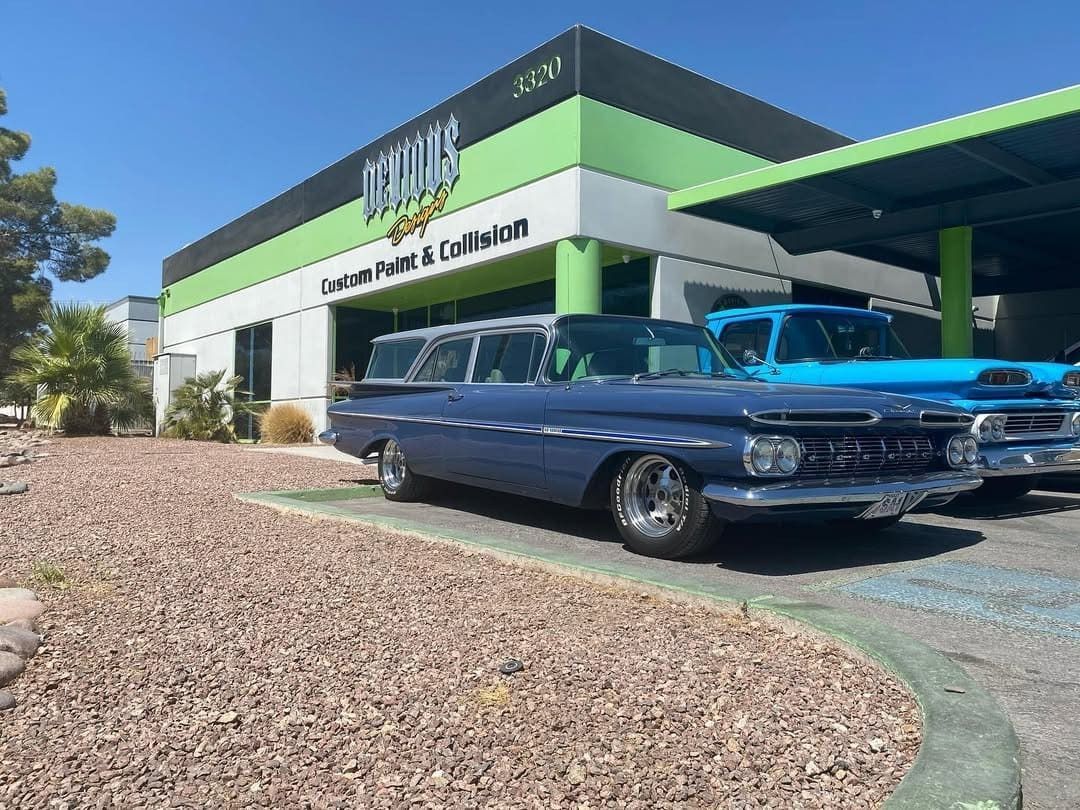 Classic blue car parked outside a green-and-white auto shop on a sunny day