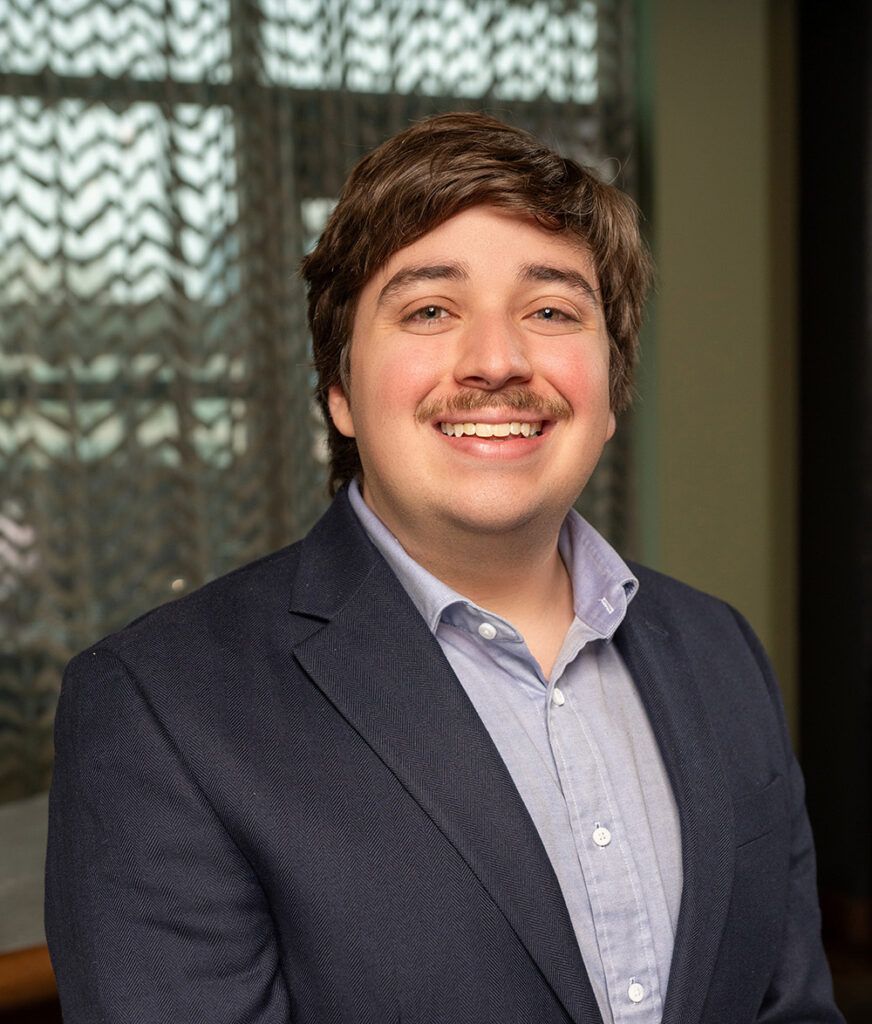 Young man in blue suit smiles at the camera.