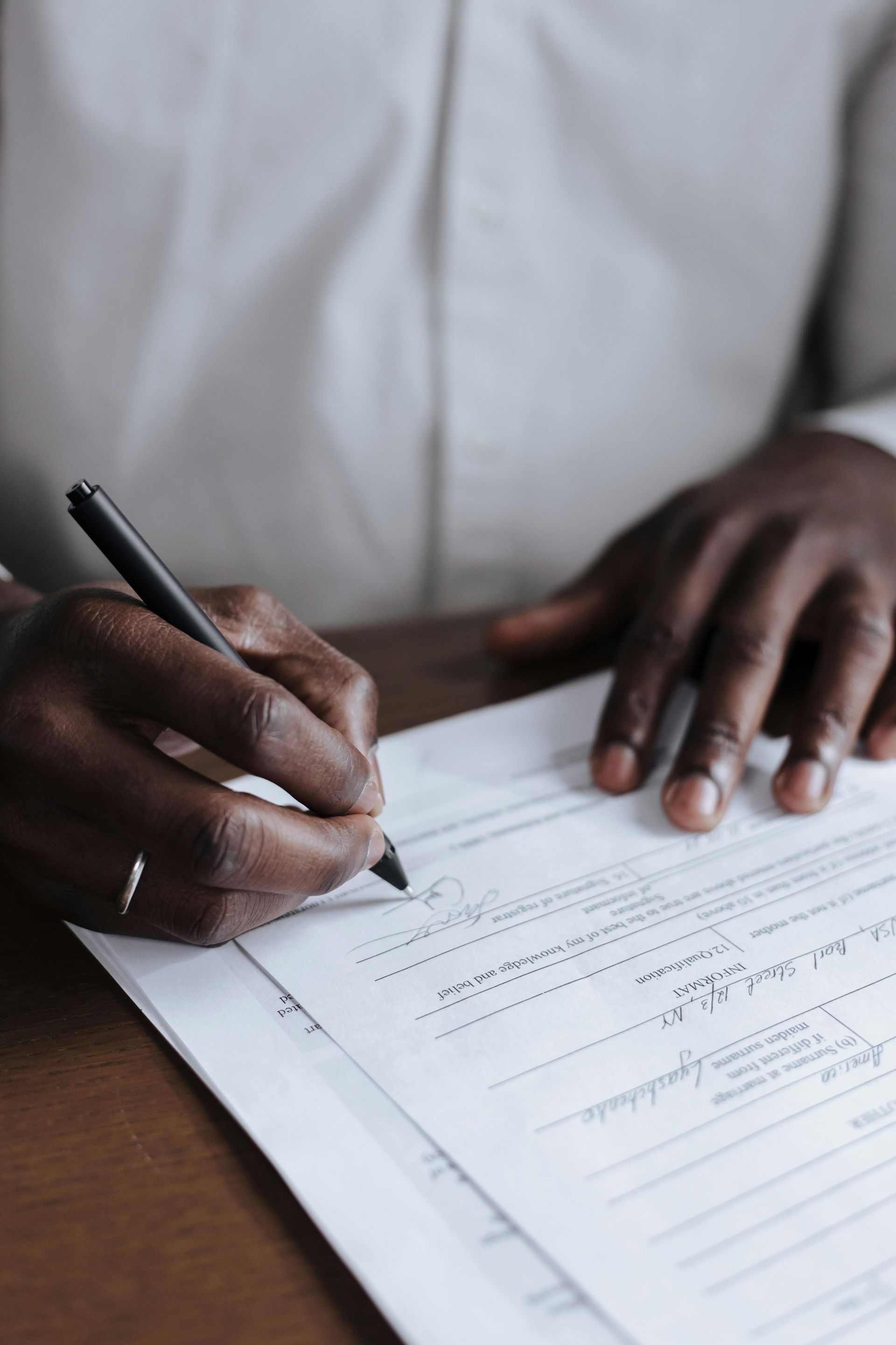 Person writing with a pen on paperwork; close-up of hands and documents.