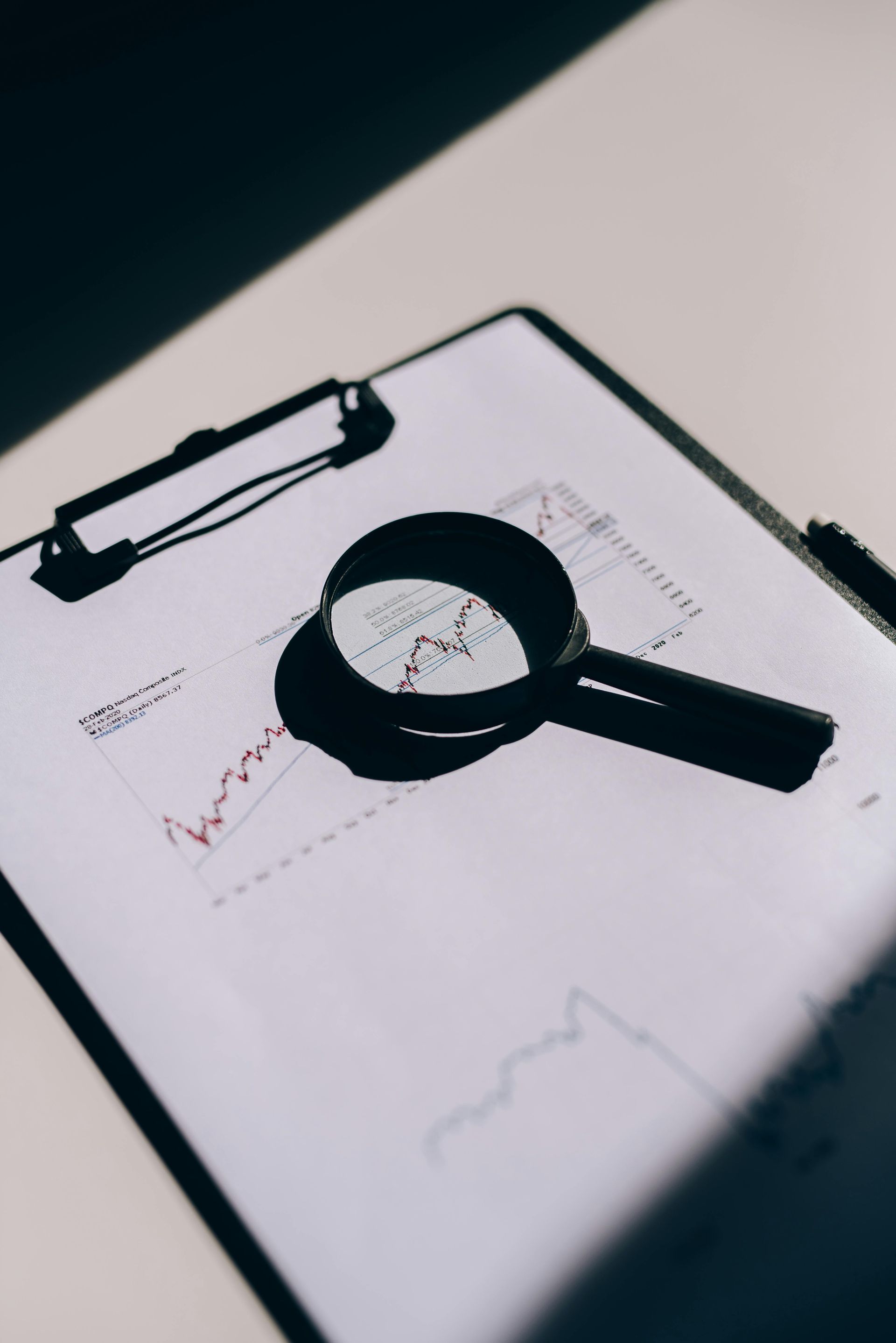 A magnifying glass is sitting on top of a clipboard with a graph on it.