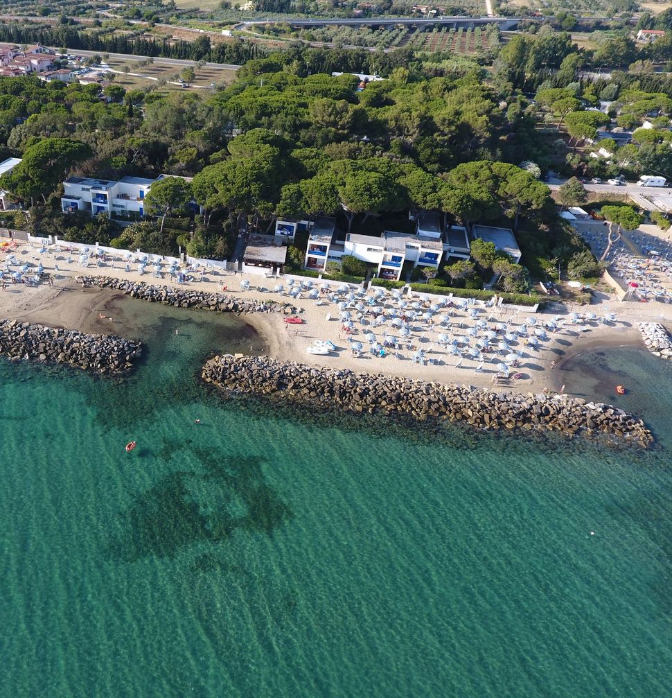 Tavoli apparecchiati per un evento sulla spiaggia, sotto ombrelloni di paglia, di fronte all'oceano.