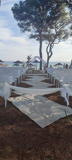 Cerimonia nuziale sulla spiaggia; sedie bianche, navata, arco, oceano sullo sfondo.
