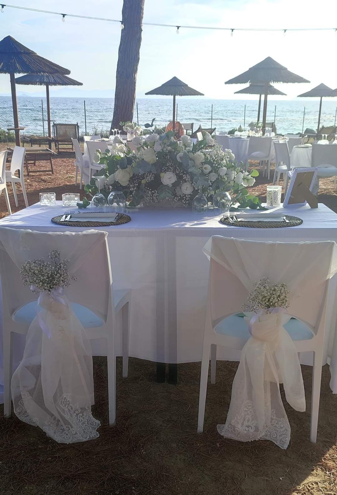 Tavolo nuziale apparecchiato sulla spiaggia. Fiori e tovaglie bianche