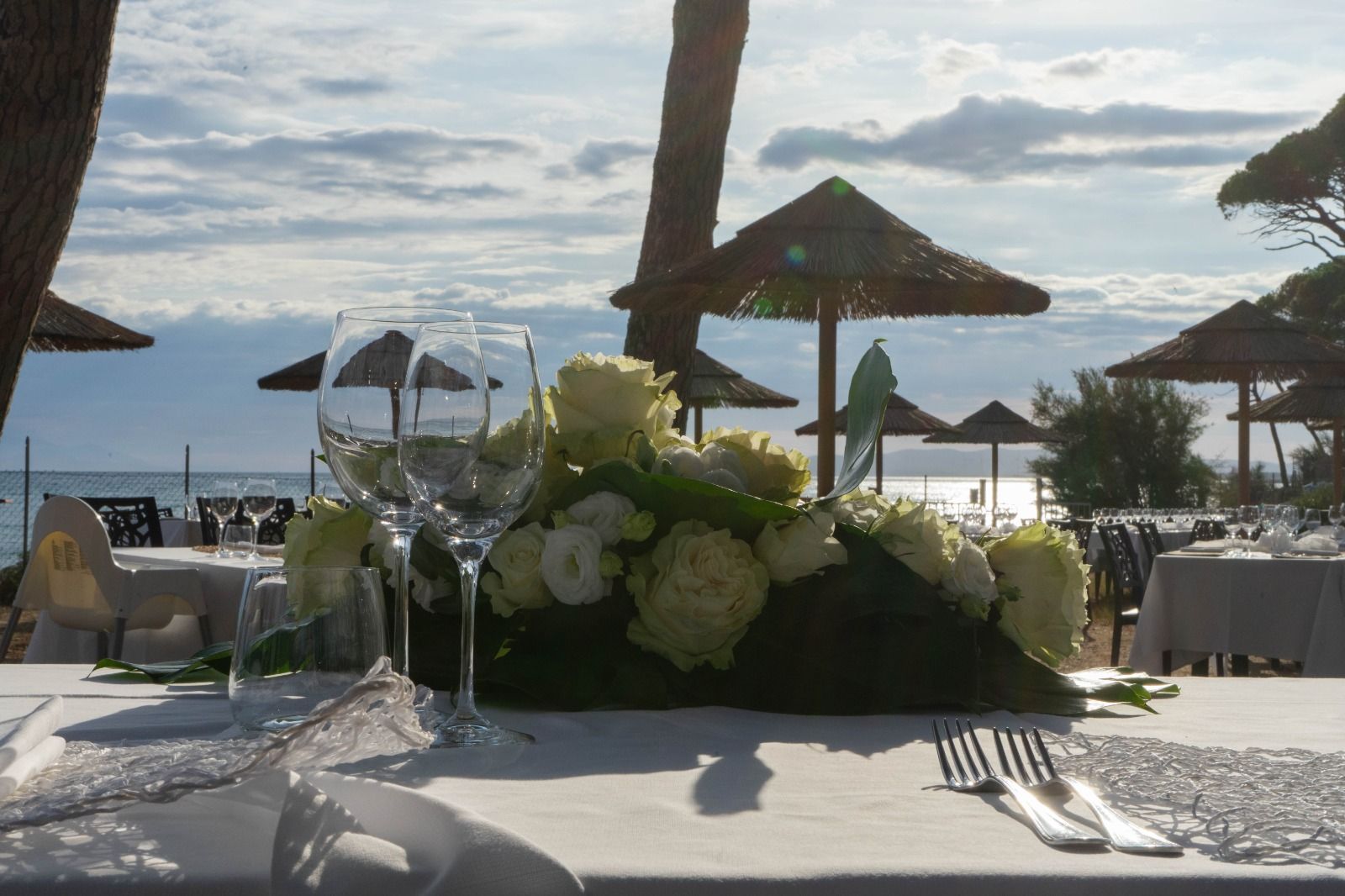 Tavolo apparecchiato in riva al mare con fiori bianchi, bicchieri e posate, vista sull'oceano.
