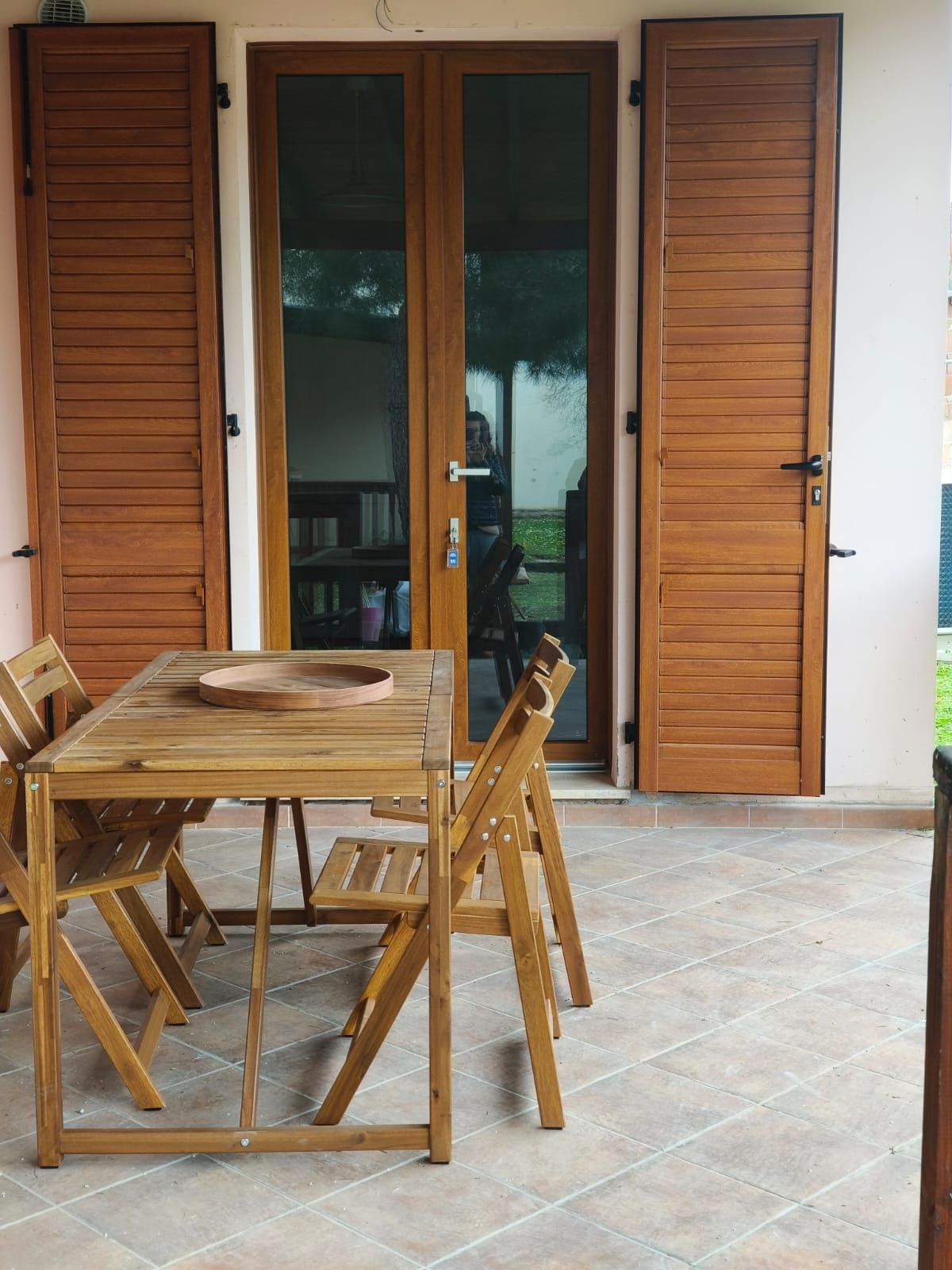 Tavolo e sedie in legno su un patio di fronte a porte marroni con persiane.