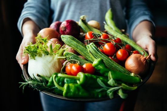 Persona che tiene in mano un vassoio pieno di varie verdure fresche e colorate.