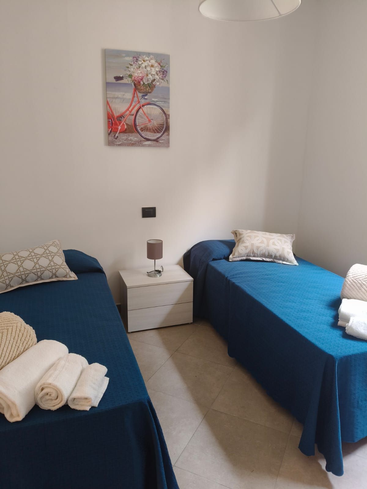 Due letti singoli con coperte blu e asciugamani bianchi in una camera da letto. Tra i due letti c'è un piccolo comodino.