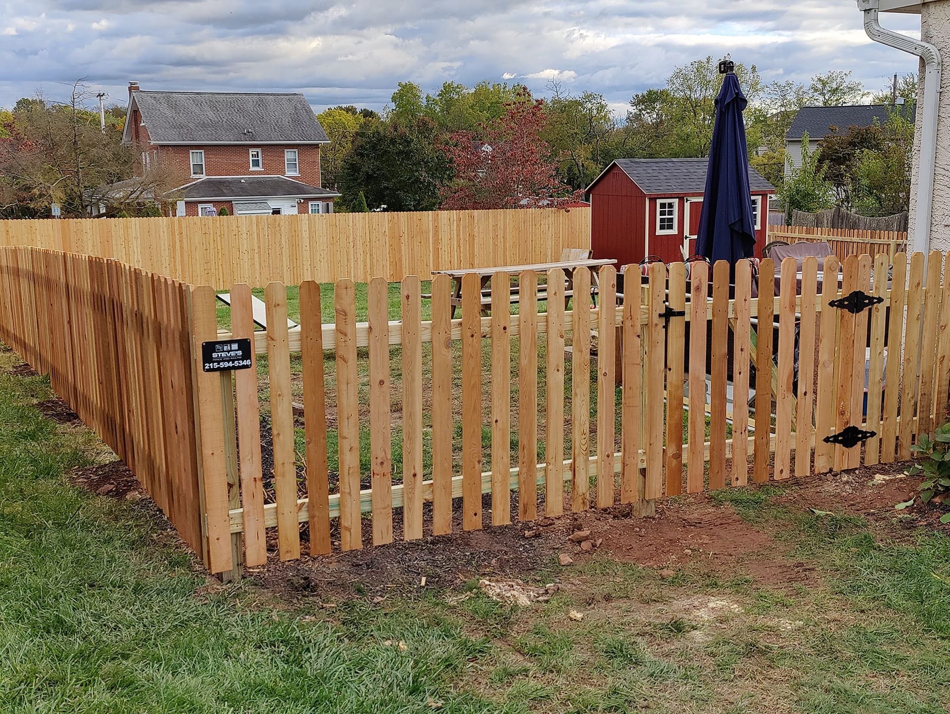 Wooden fenced yard with a gate, patio umbrella, and houses in the background.