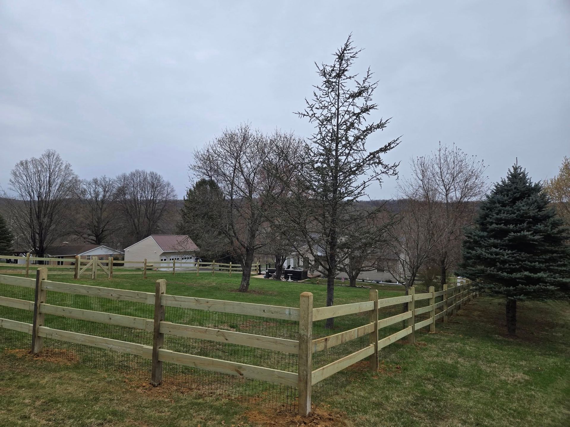 A wooden fence surrounds a grassy field with trees in the background.