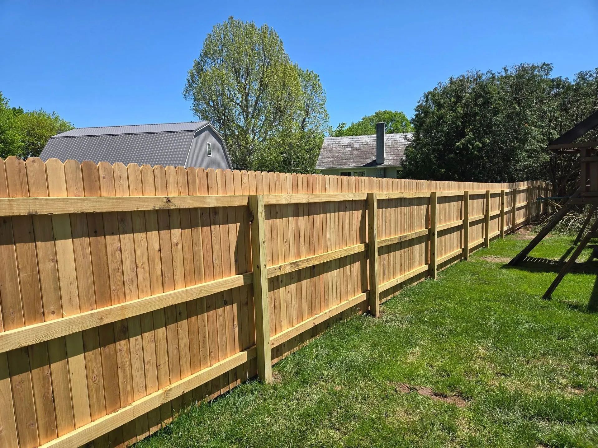 Wooden backyard fence along a green lawn under a sunny blue sky