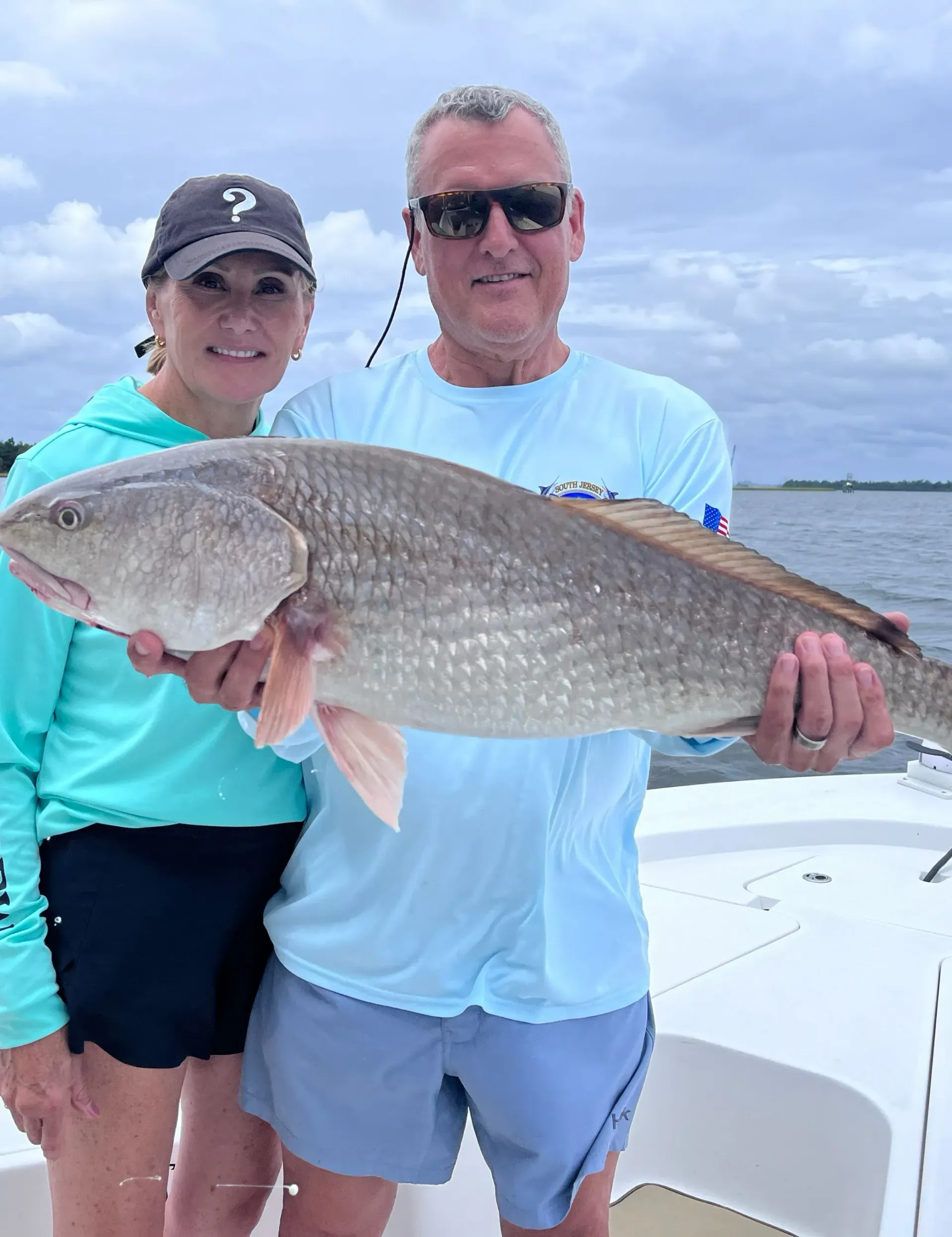 A man and a woman are holding a large fish on a boat.