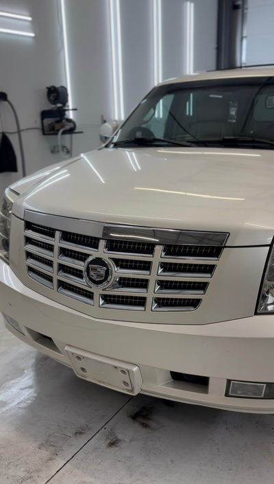 A front-angle view of a white Cadillac SUV parked inside a brightly lit garage or shop.