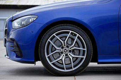 A bright blue Mercedes-Benz car showing the front fender, headlight, and detailed alloy wheel.