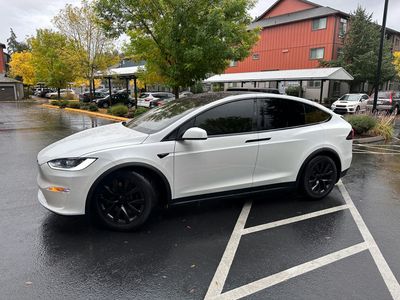 A white Tesla Model X with black rims parked in a wet parking lot during the day.