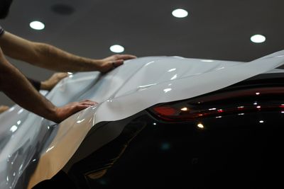 A person in black gloves applies a clear protective film to the rear panel of a bright orange car.