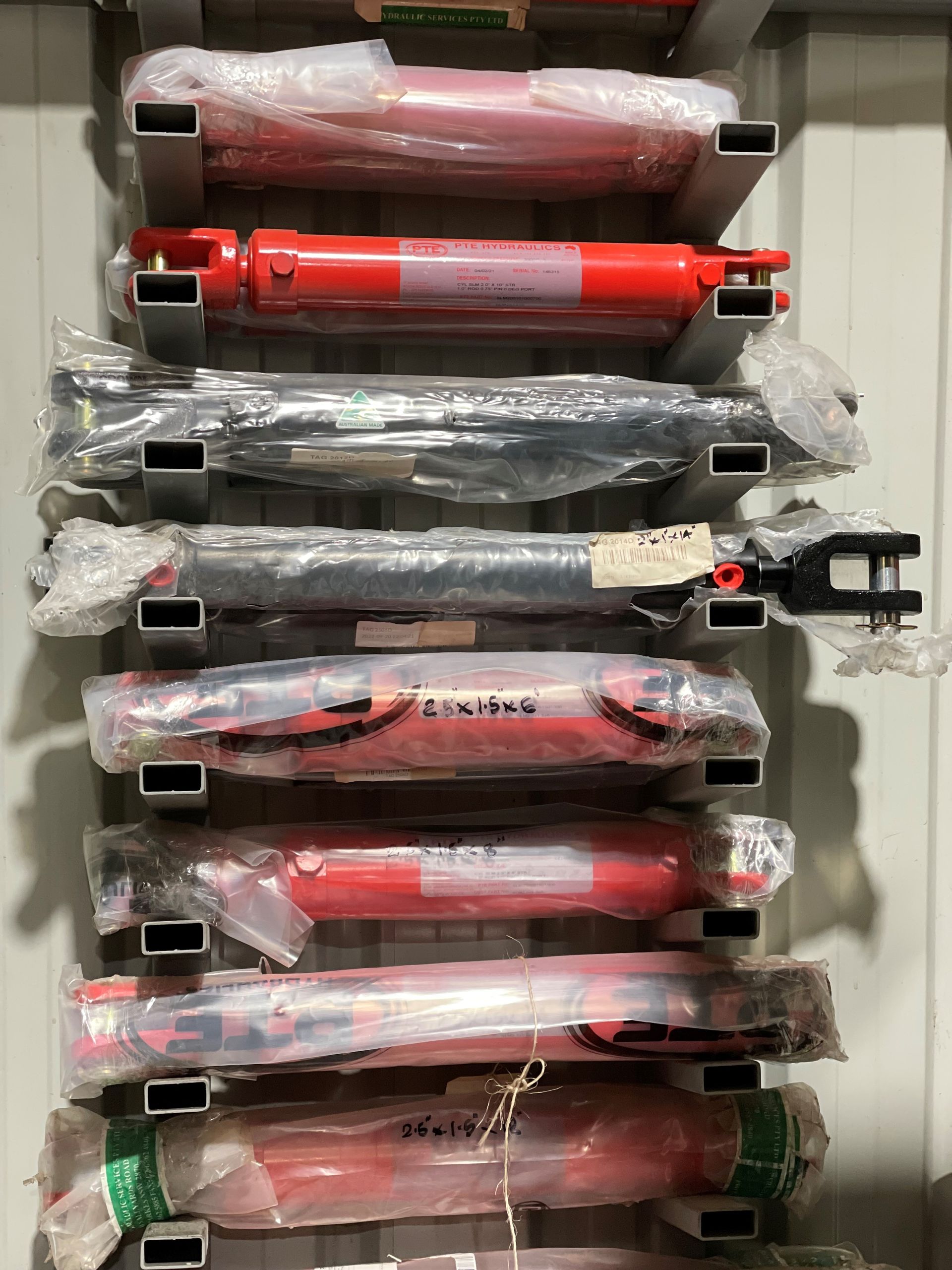 A row of red hydraulic cylinders stacked on top of each other on a rack.