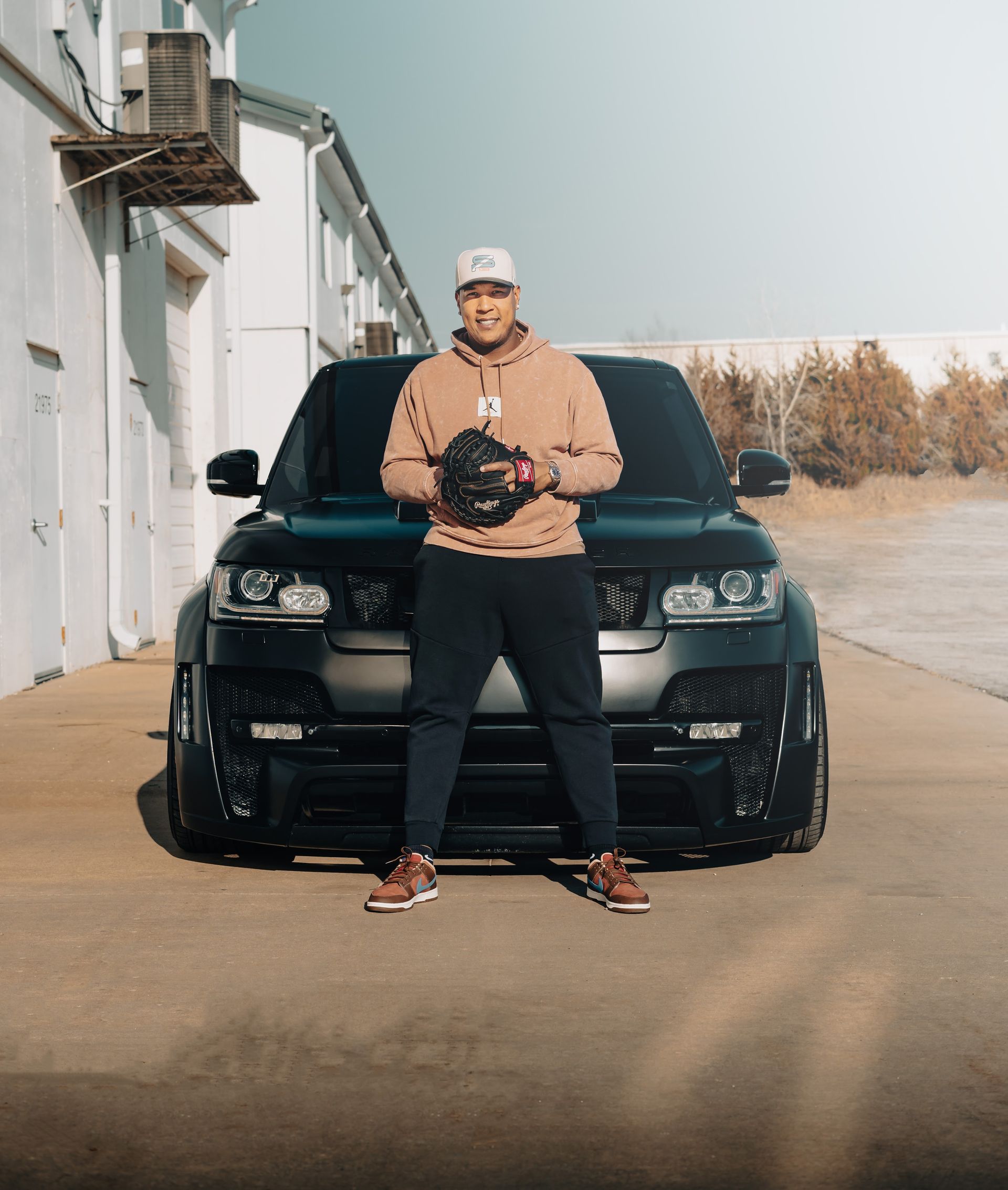 Person standing in front of a black SUV on an industrial street, holding a camera.