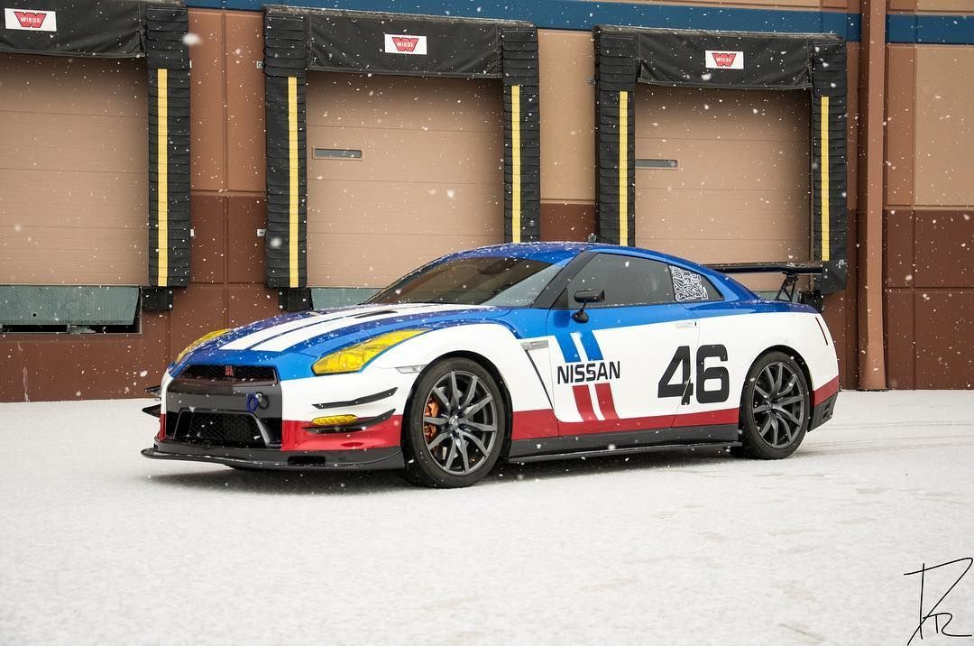 Race car number 46, white with blue and red accents, parked in front of garage doors in the snow.