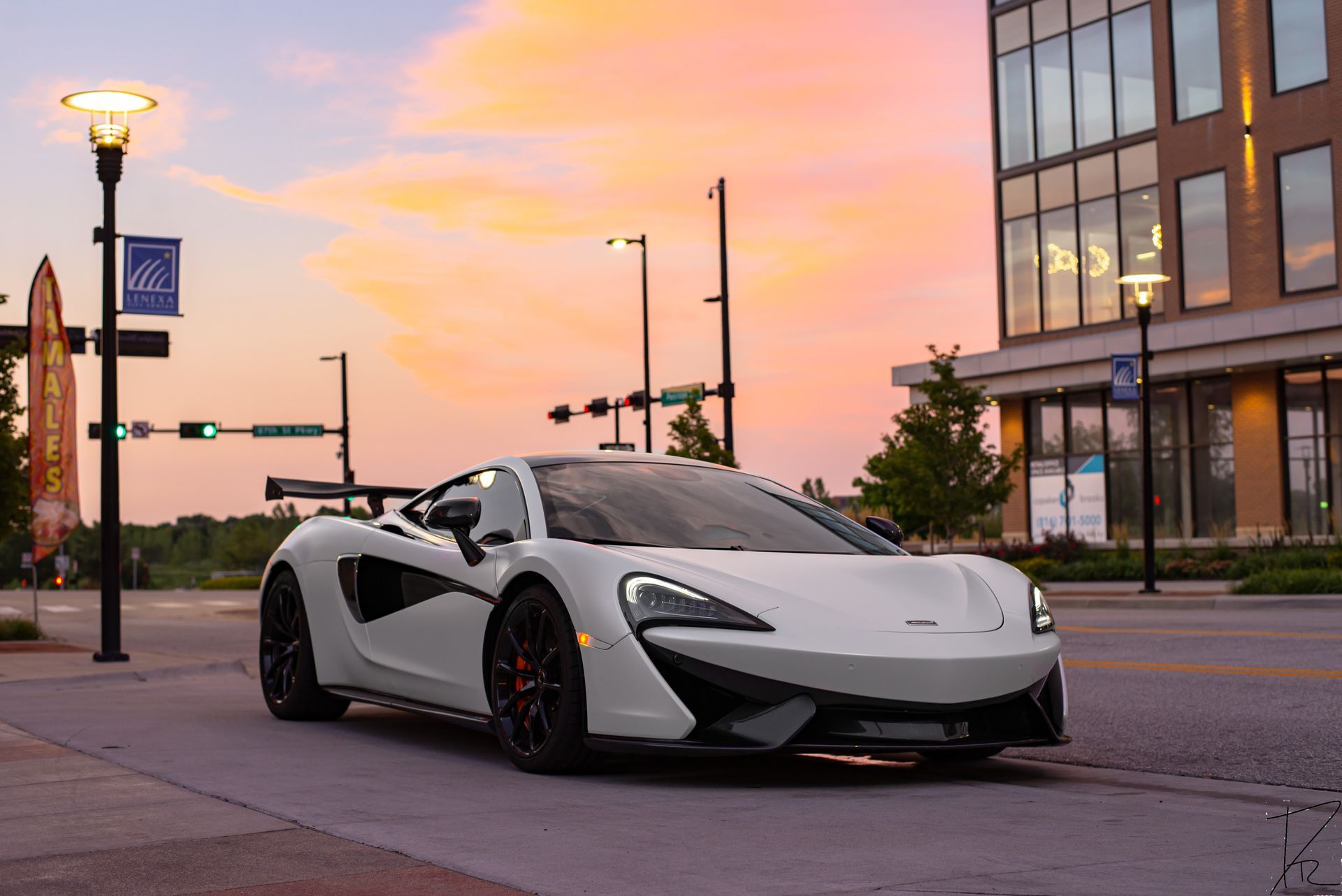 White sports car parked on a city street at sunset beside a modern glass building