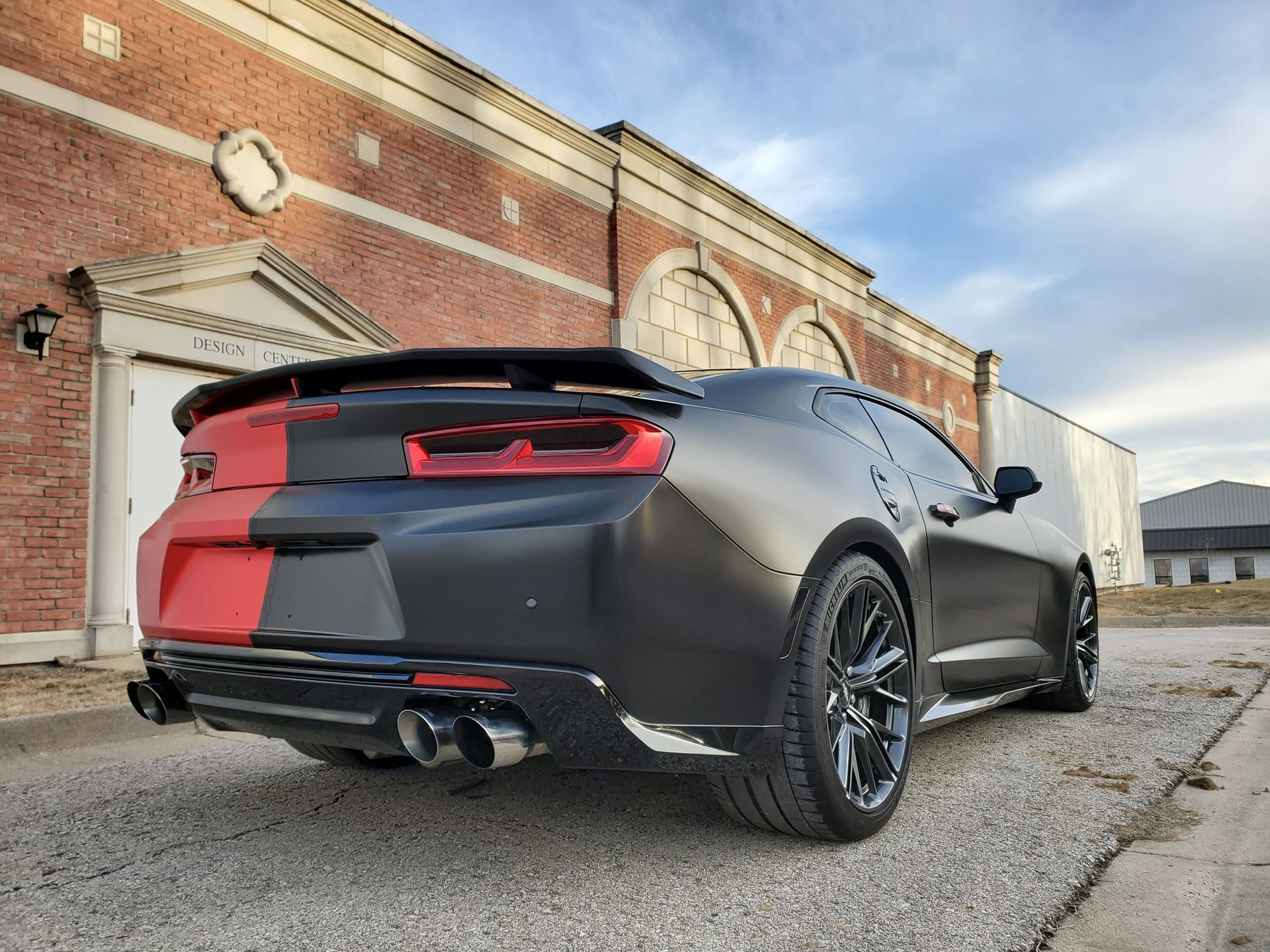 Black sports car parked beside a brick building on a street, rear view.