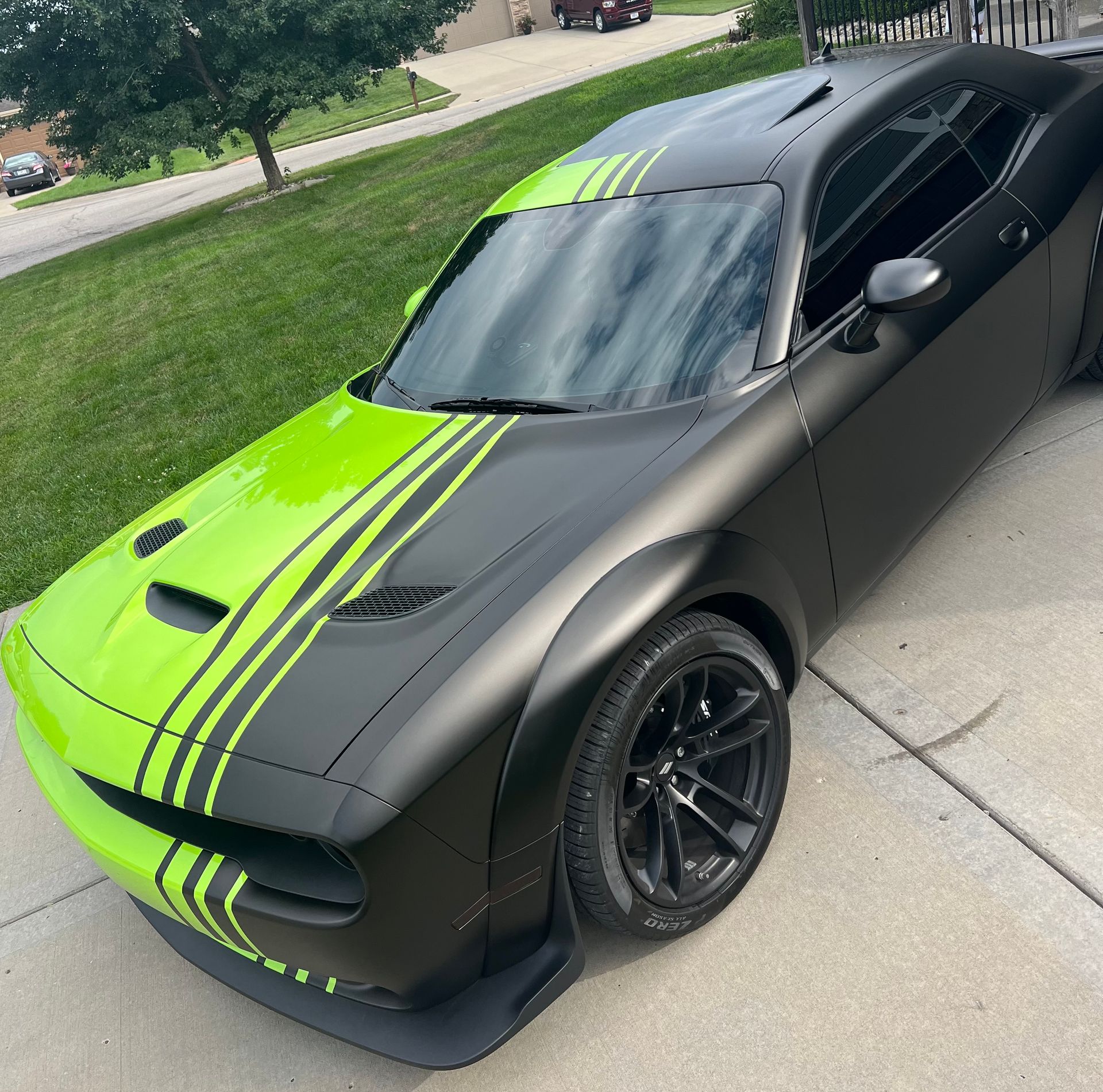 Black sports car with neon green racing stripes parked on a driveway.