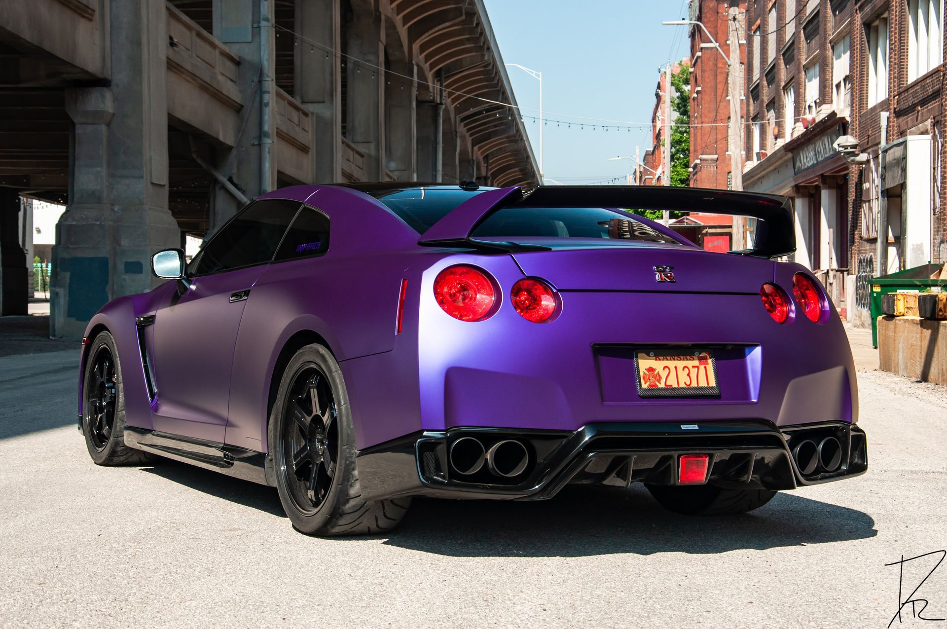 Purple Nissan GT-R sports car parked on a city street under an elevated roadway, rear view.