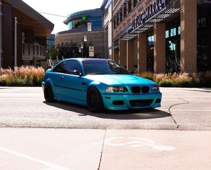 Bright turquoise sports sedan parked outside a brick building on a sunny street.