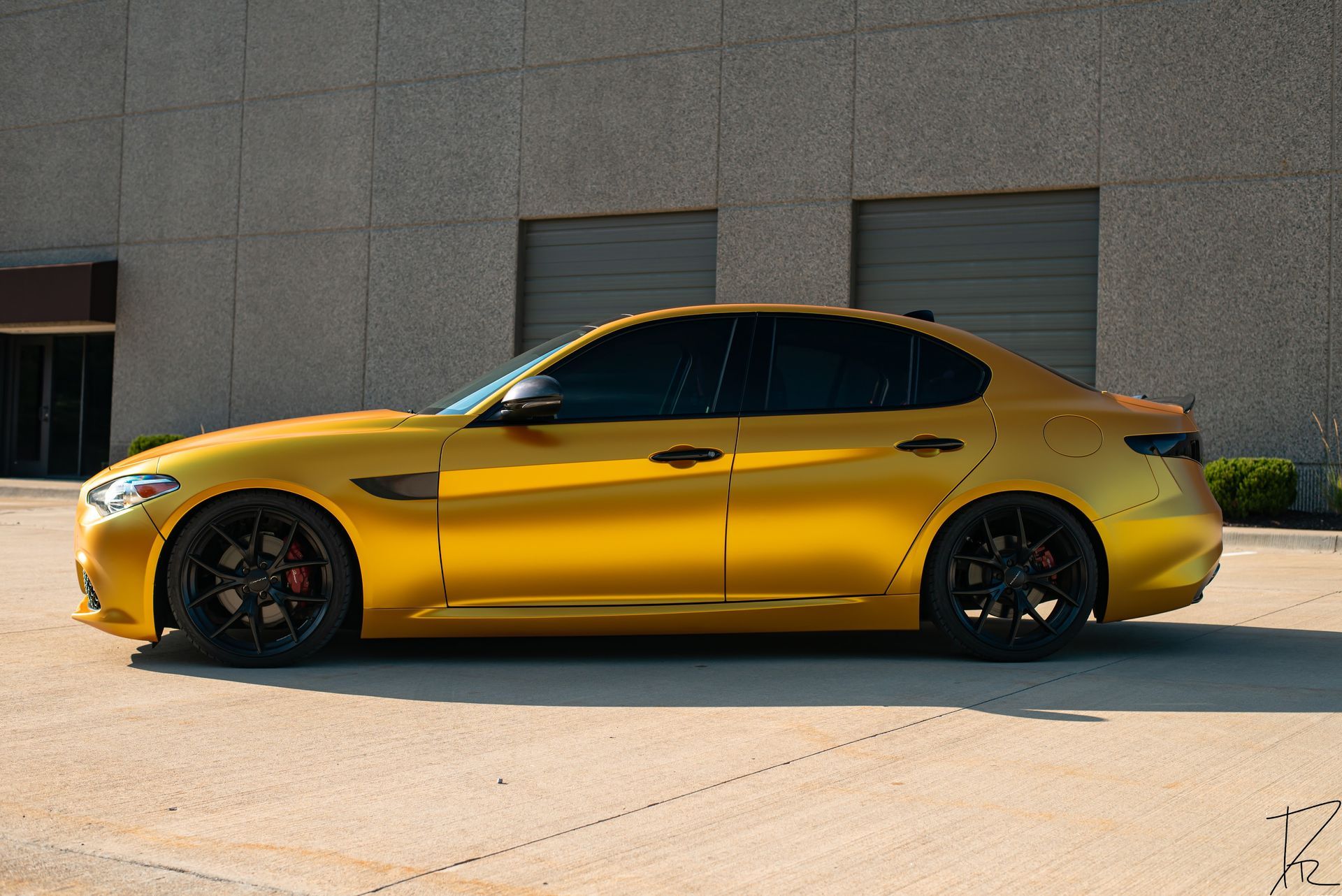 Yellow sports sedan parked beside a concrete building in bright sunlight.