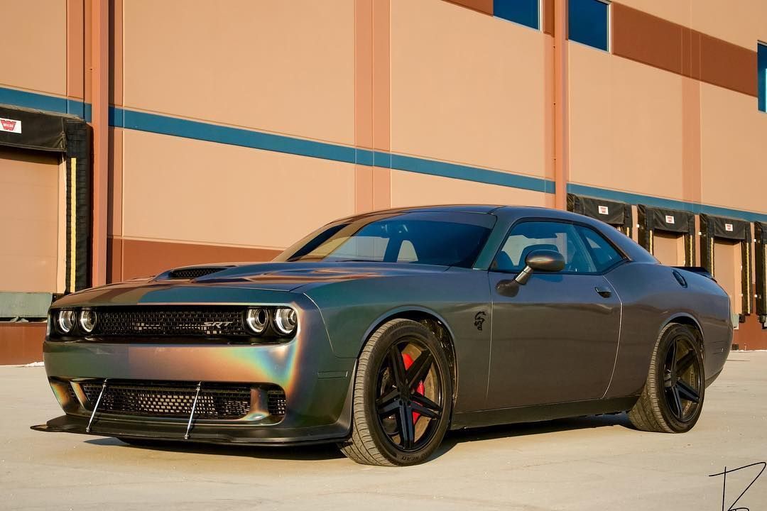 Dark gray sports car parked beside a tan wall in bright sunlight