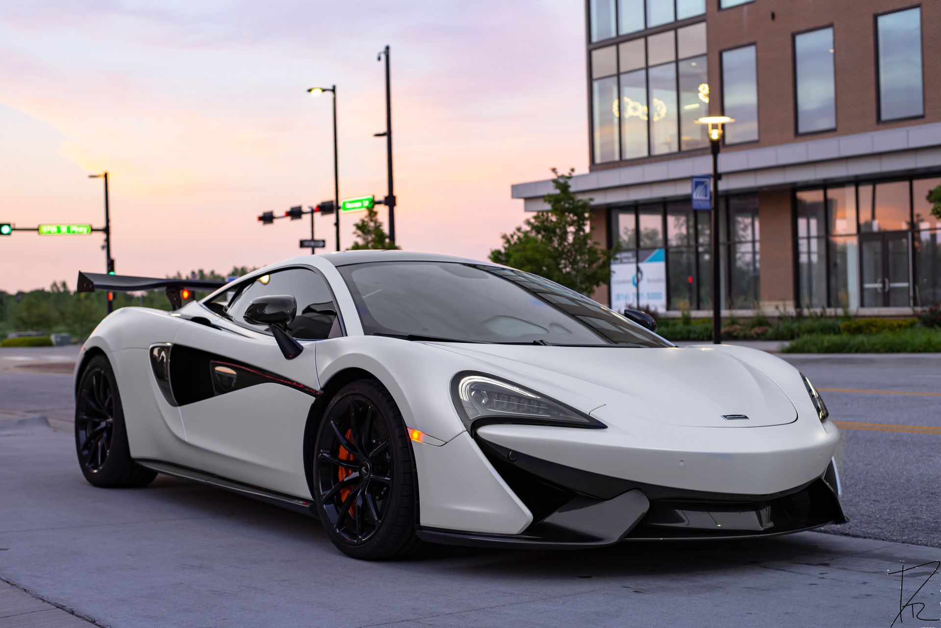 White McLaren supercar parked on a street at dusk outside a modern building