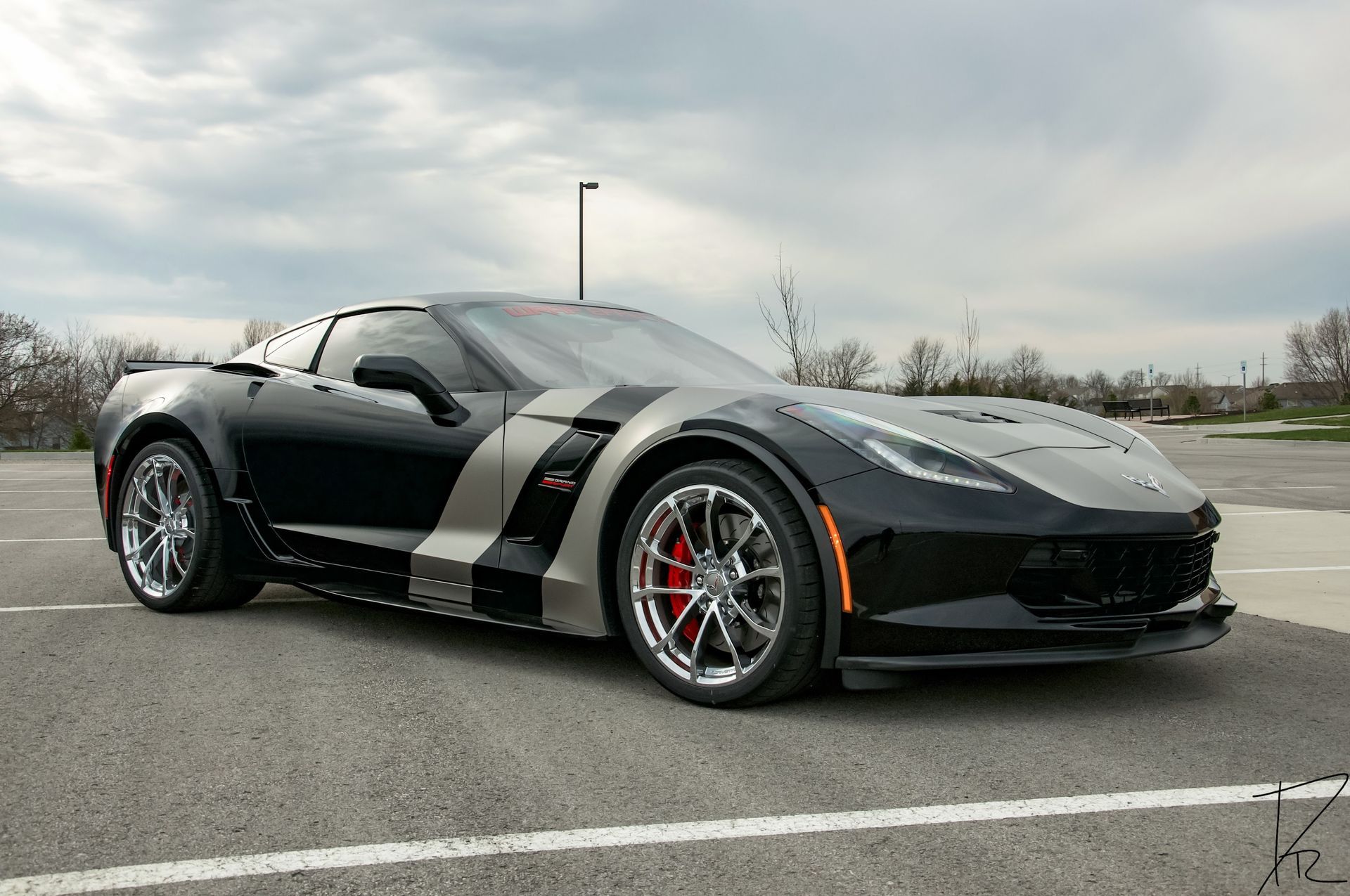 Black sports car with silver racing stripes parked on a road under a cloudy sky