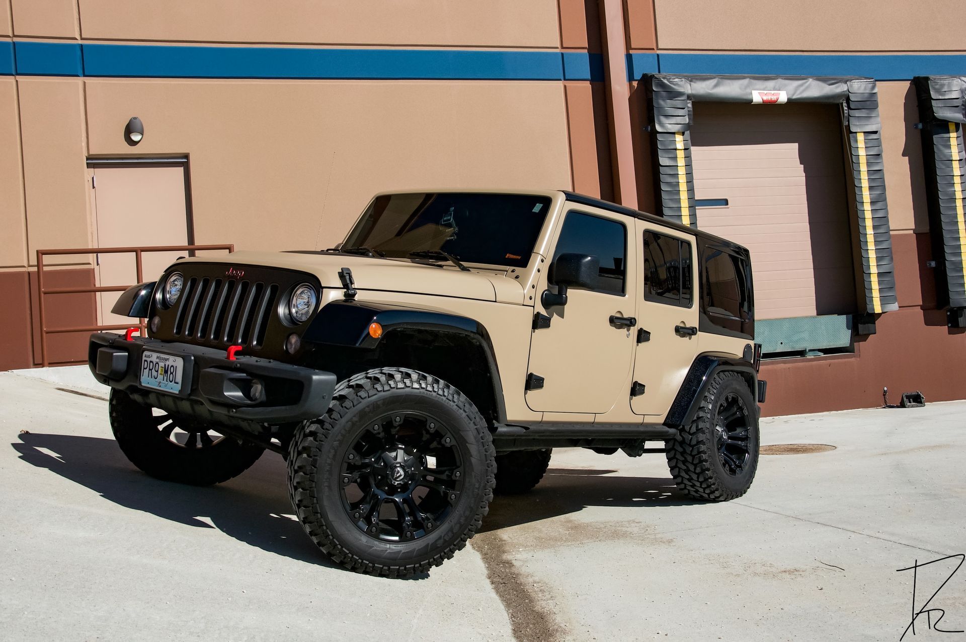Tan Jeep Wrangler with black wheels parked outside a building in bright sunlight