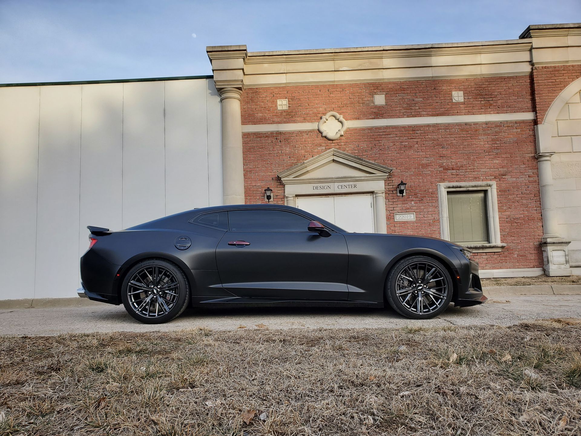 Matte black sports car parked beside a brick building with a white wall