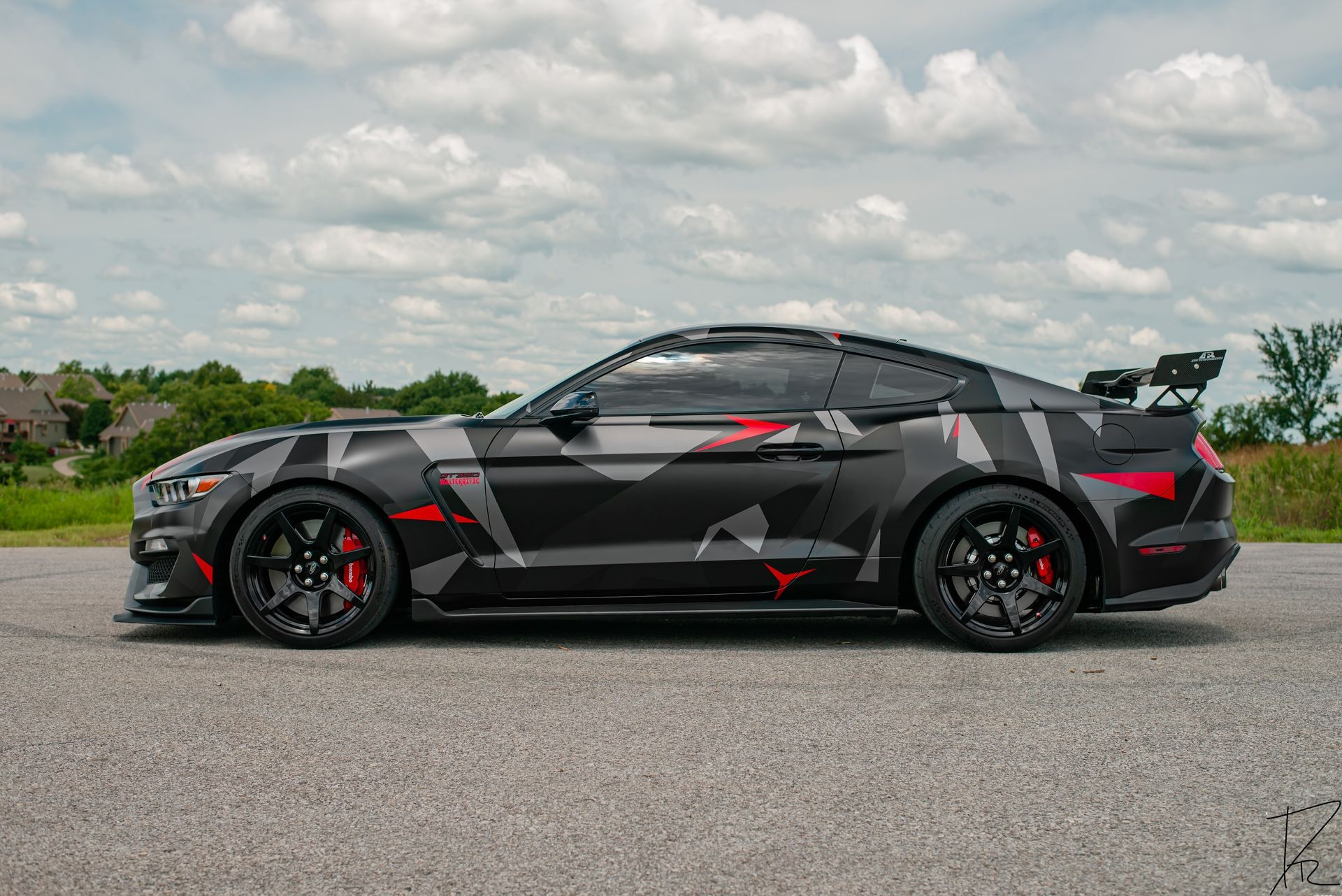 Black sports sedan with red accents parked on a road under a cloudy sky