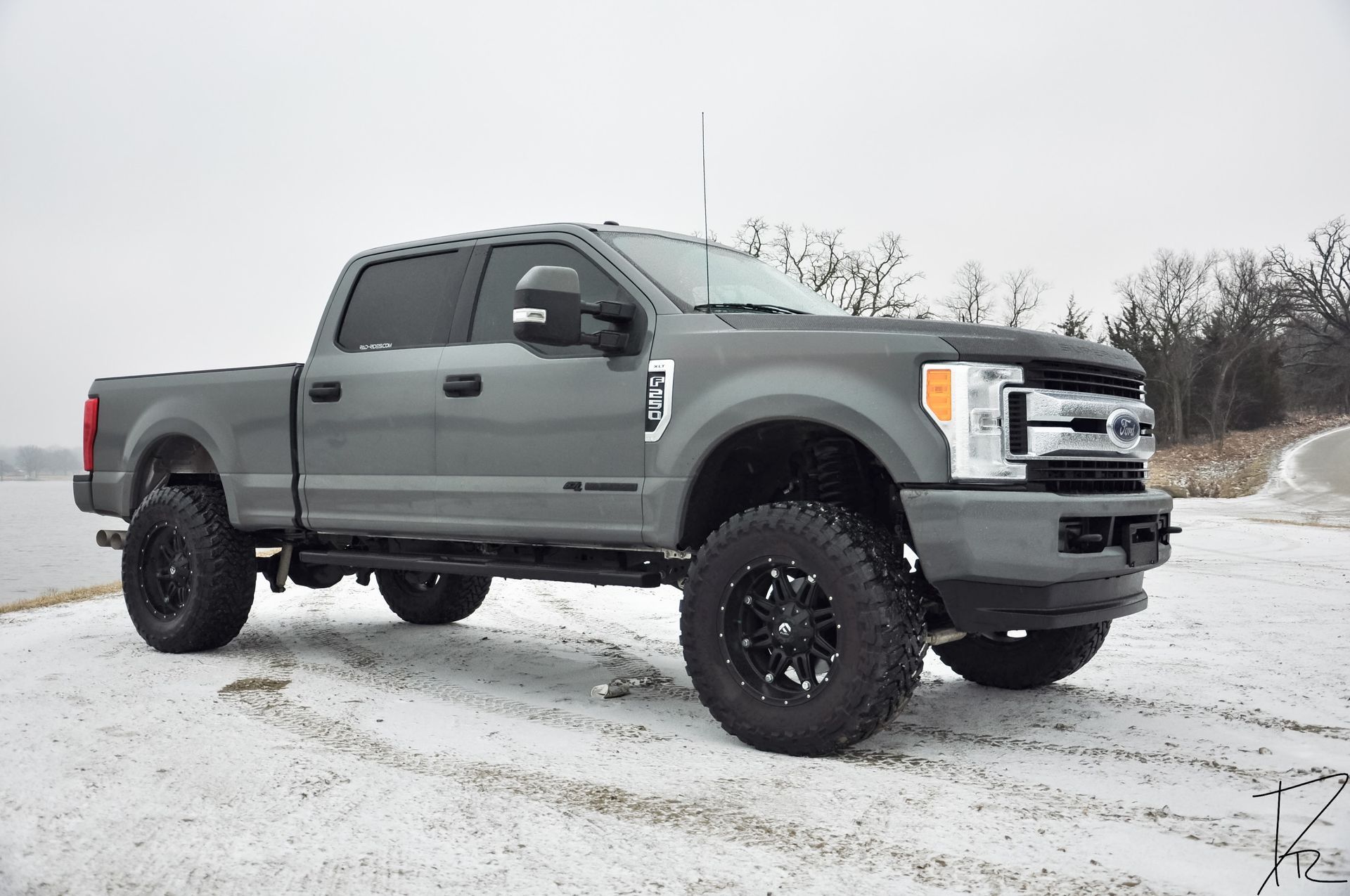 Gray lifted pickup truck parked on a snowy lot under an overcast sky