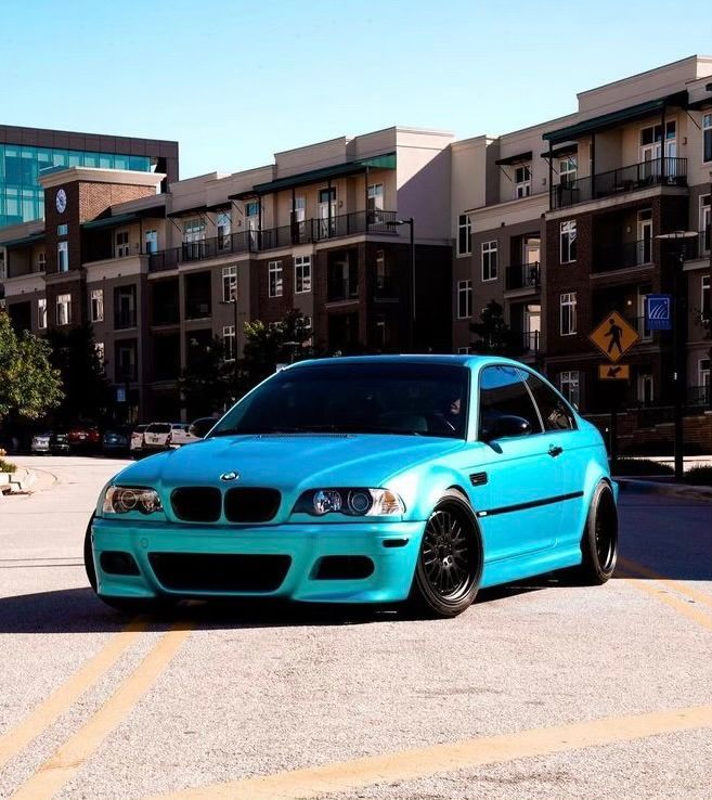 Bright turquoise BMW parked on a city street in front of apartment buildings