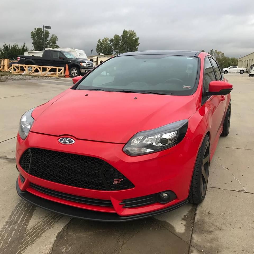 Red Ford hatchback parked on a concrete lot under cloudy skies.